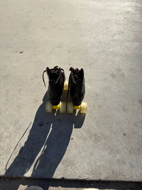Black roller skates with yellow wheels and a long shadow on concrete